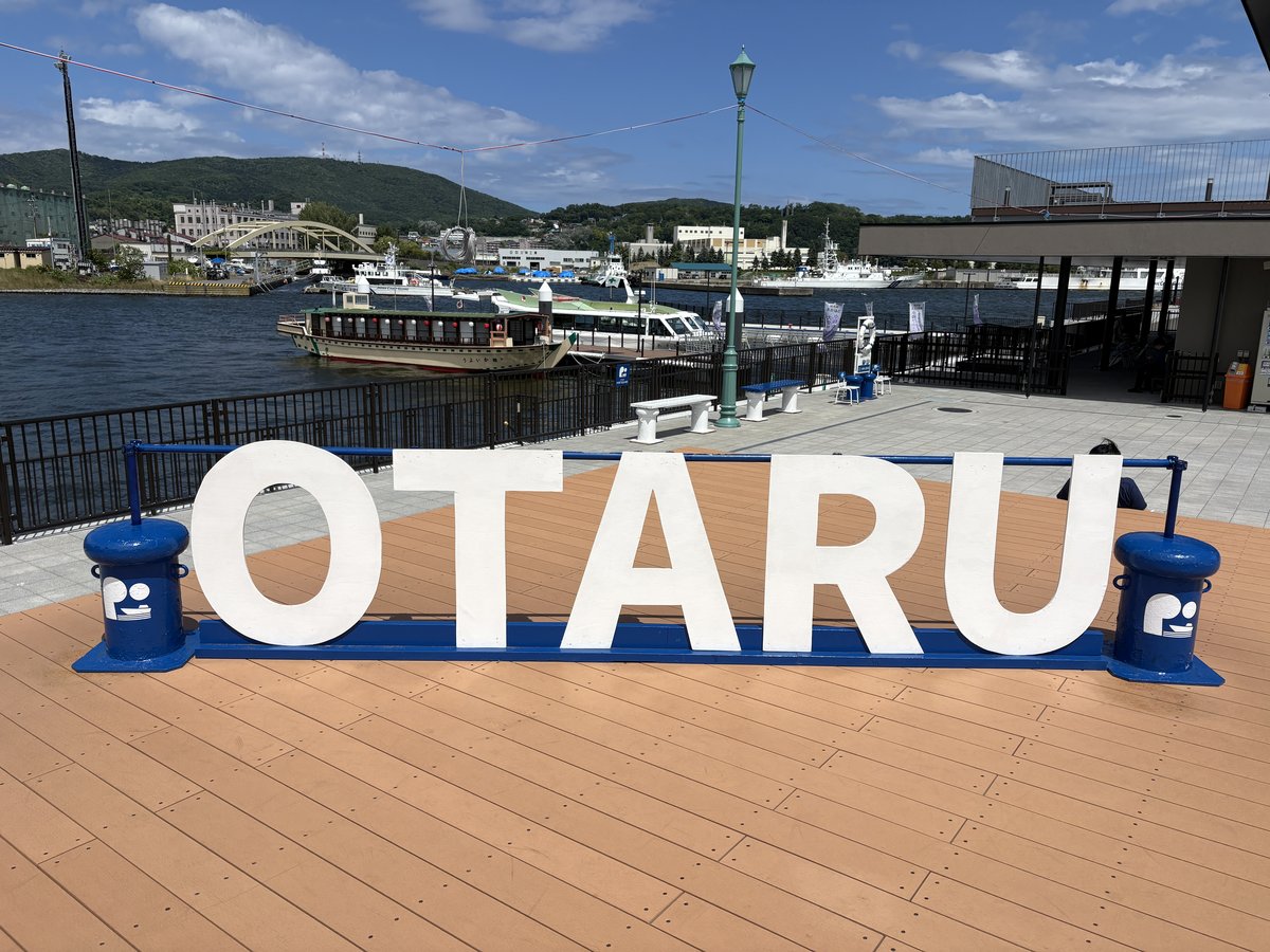 小樽港と停泊する船を背景に置かれた、白い「OTARU」の文字のモニュメント