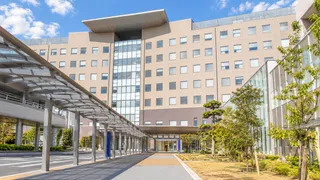 秋の青空の下に建つ病院と、正面玄関へ続く屋根付きの通路
